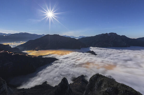 A night view with full moon on Lecco and Valsassina wrapped up by the clouds from the top of Coltignone mount, lake Como, lecco province, Lombardy, Italy, Europe