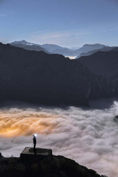 Hiker looks the sky in a night with full moon with Lecco wrapped up by the clouds, view from the top of Coltignone mount, lake Como, lecco province, Lombardy, Italy, Europe (MR)