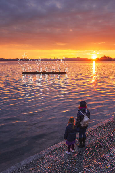 Mom and son looks a Christmas sunset on Pusiano lake with the lights of floating nativity scene, Pusiano, Brianza, Como province, Lombardy, Italy, Europe (MR)