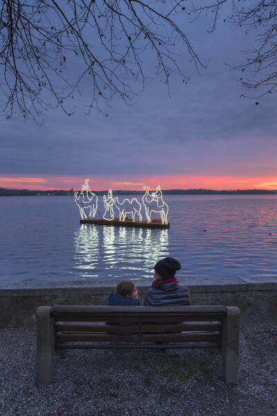 Mom and son have fun in front of Pusiano lake with the lights of floating nativity scene, Pusiano, Brianza, Como province, Lombardy, Italy, Europe (MR)