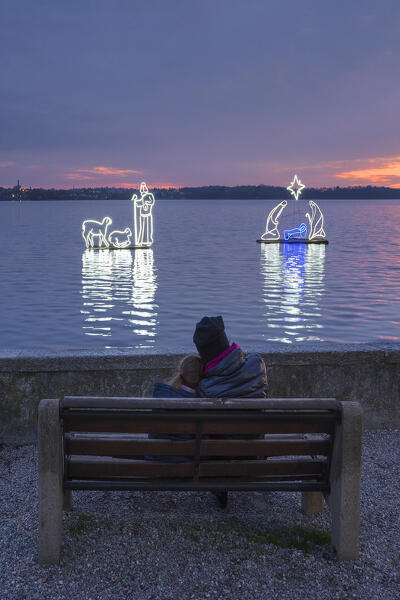 Mom and son relaxes look at the lights of floating nativity scene on Pusiano lake, Pusiano, Brianza, Como province, Lombardy, Italy, Europe (MR)