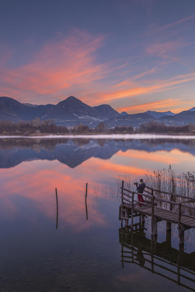 A photographer on the pier capture a sunrise from Alserio lake, Parco regionale della Valle del Lambro, Brianza, Como province, Lombardy, Italy, Europe (MR)