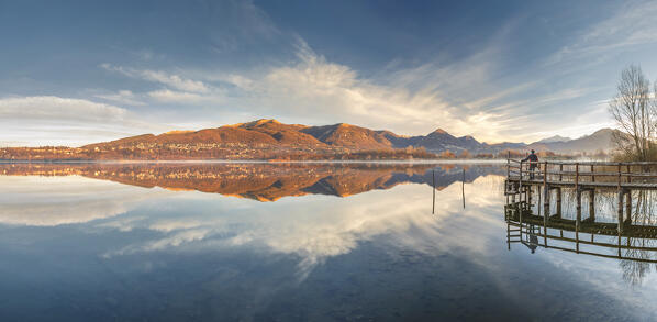 Panoramic view of the hiker on the pier that looks reflections of Alserio lake, Parco regionale della Valle del Lambro, Brianza, Como province, Lombardy, Italy, Europe (MR)