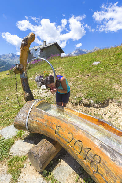 Hiker take rest drinking a water on the fountain, Altopiano degli Andossi, Madesimo, Spluga valley, Sondrio province, Lombardy, Italy, Europe (MR)