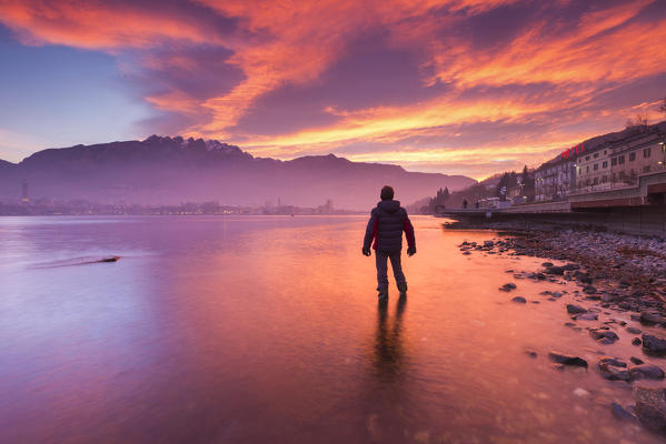 Man into the water admire a fire sunrise on Lecco and mountains, lake Como, Lombardy, Italy, Europe (MR)