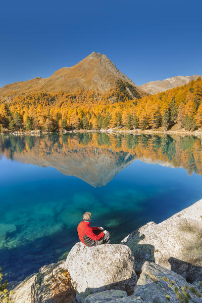 Hiker take a break to admire lake Saoseo in autumn time, Poschiavo, val di Campo, Canton of Graubunden, Switzerland, Europe (MR)