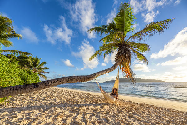 A woman relaxing on a hammock at sunrise. La Digue, Seychelles, Africa (MR)