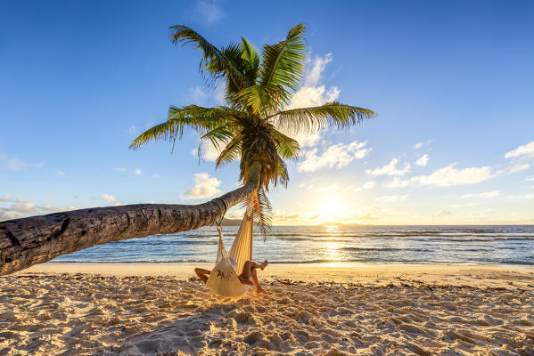 A woman relaxing on a hammock at sunrise. La Digue, Seychelles, Africa (MR)