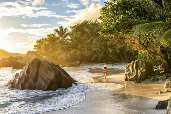 A young woman enjoys the sunrise on Anse Patates beach. La Digue, Seychelles, Africa (MR)