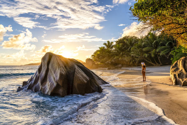 A young woman enjoys the sunrise on Anse Patates beach. La Digue, Seychelles, Africa (MR)