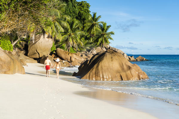 A couple walking along Anse Patates beach. La Digue, Seychelles, Africa (MR)