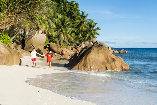 A couple walking along Anse Patates beach. La Digue, Seychelles, Africa (MR)