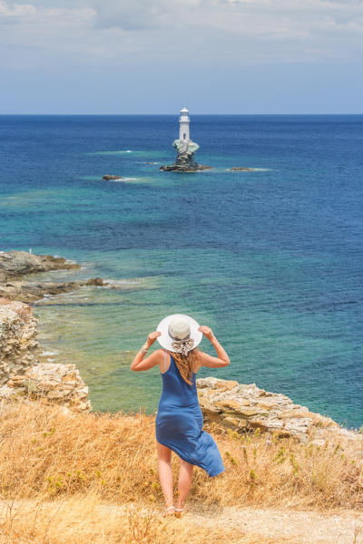 Young woman admiring the enchanting offshore Tourlitis lighthouse, Andros, Cyclades Archipelago, Greece, Europe