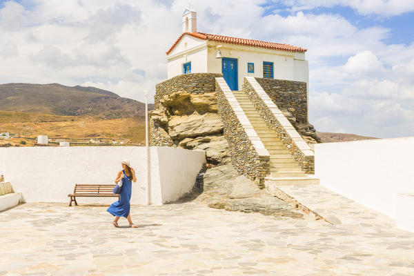 Young woman in a blue dress walking near St, Thalassini Church in a windy day, Andros, Cyclades archipelago, Greece, Europe (MR)