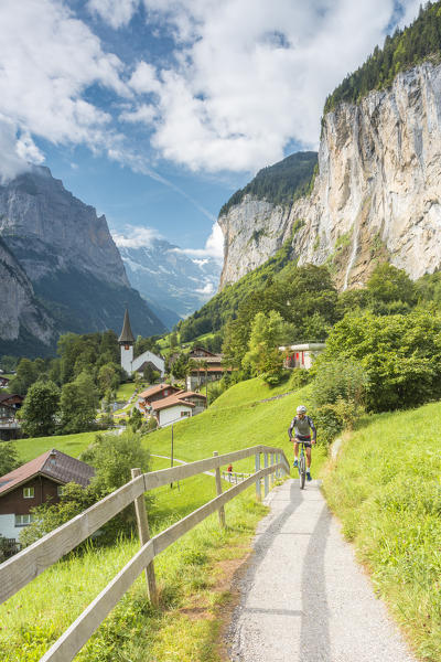 A bikers crossing a street of Lauterbrunnen with Staubbach Fall in the background,Interlaken-Oberhasli administrative district, canton of Bern,Bernese Oberland, Switzerland.