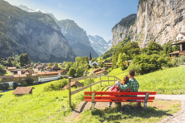 Two lovers on a red bench admiring the village of Lauterbrunnen,Interlaken-Oberhasli administrative district, canton of Bern,Bernese Oberland, Switzerland.