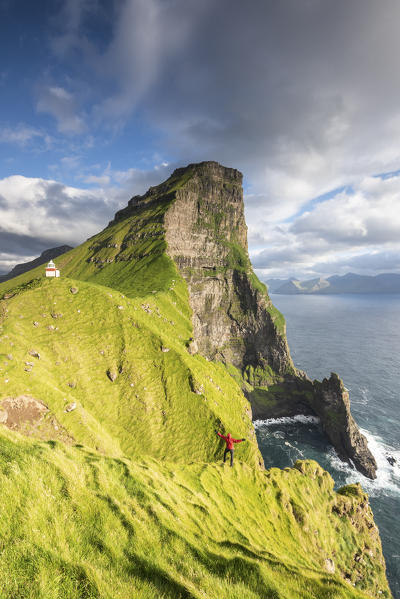 Hiker runs on steep cliffs at Kallur lighthouse, Kalsoy island, Faroe Islands, Denmark