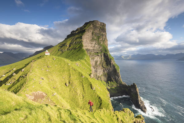 Hiker runs on steep cliffs at Kallur lighthouse, Kalsoy island, Faroe Islands, Denmark
