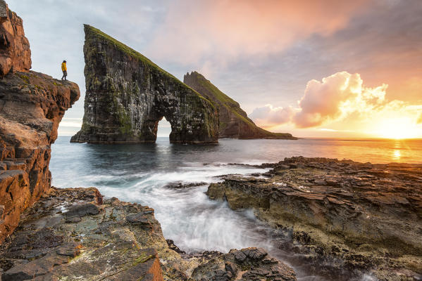 Hiker is admiring the sunset in front of the rock of Drangarnir, Vagar Island, Faroe Islands, Denmark