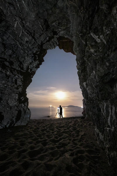a night landscape photographer is photographed from inside a cave on a beach, municipality of Ameglia, La Spezia province, Liguria district, Italy, Europe