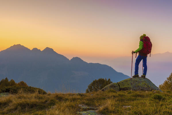 Hiker admiring sunset from Alpe Torrenzuolo, Val Tartano, Orobie alps, Valtellina, Sondrio province, Lombardy, Italy