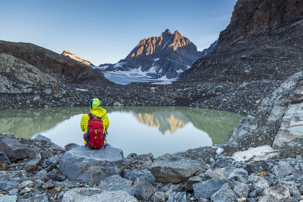Hiker looks at Piz Roseg from the epiglacial lake next to Fellaria Glacier, Malenco Valley, Sondrio Province, Valtellina, Lombardy, Italy