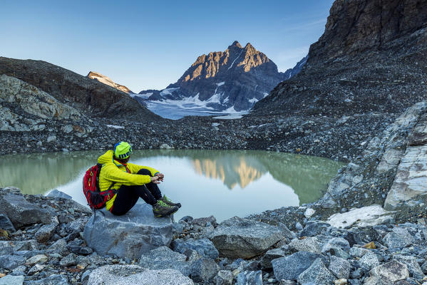 Hiker looks at Piz Roseg from the epiglacial lake next to Fellaria Glacier, Malenco Valley, Sondrio Province, Valtellina, Lombardy, Italy