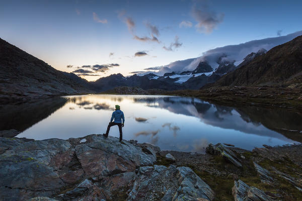 Hiker admiring Piz Argent and Zupò from lake Confinale, Valmalenco, Valtellina, Sondrio province, Lombardy, Italy