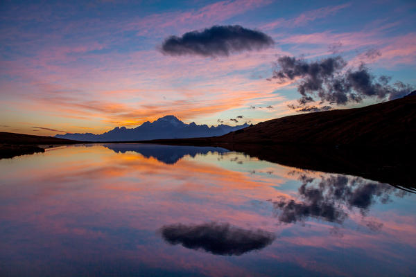 Clouds are reflected in the lake of Campagneda at sunset, in the background Disgrazia mountain, Malenco valley, Lombardy, Italy