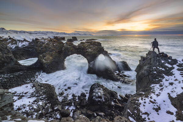 A photographer at Gatklettur arch during winter sunrise, Arnarstapi, Hellnar,  Snæfellsnes Peninsula, Iceland, Northern Europe (MR)