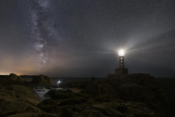 A man with a torch observes an illuminated Punta Nariga lighthouse at night with milkyway, Costa da Morte, Galicia, Spain, Iberian Peninsula, Western Europe