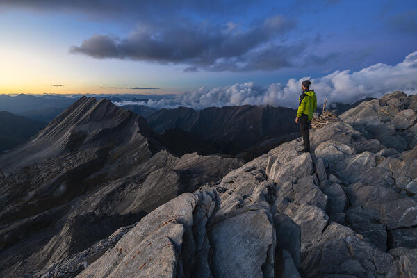 A trekker observes Crete de la Taillante from Pain de Sucre during dusk at summer, Pain de Sucre, Col Agnel, Alpi Cozie, Cuneo, Provance, Piedmont, France, Italy, Southern Europe