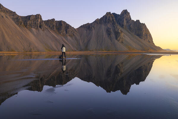 A photographer at Vestrahorn reflected in the black sand beach at sunrise, Stokksnes peninsula, Hofn, Austurland, Iceland , Northern Europe
