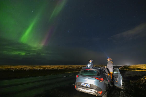 Two guys observe Northern lights along the road to the south coast from their car, Iceland, Northern Europe