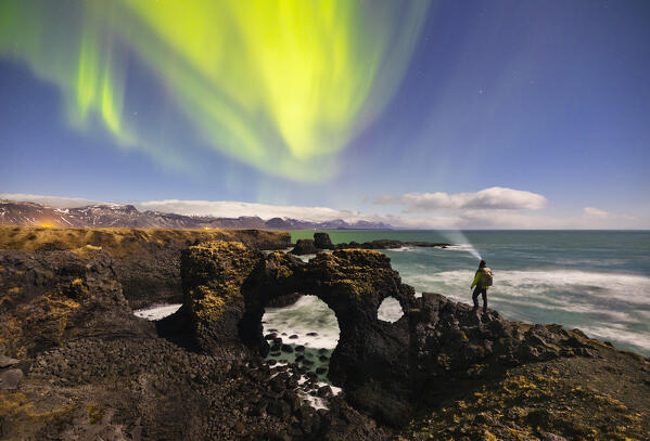 A man observes Gatklettur arch and northern lights, Arnarstapi, Snaefellsnes peninsula, Vesturland region, Iceland, Northern Europe
