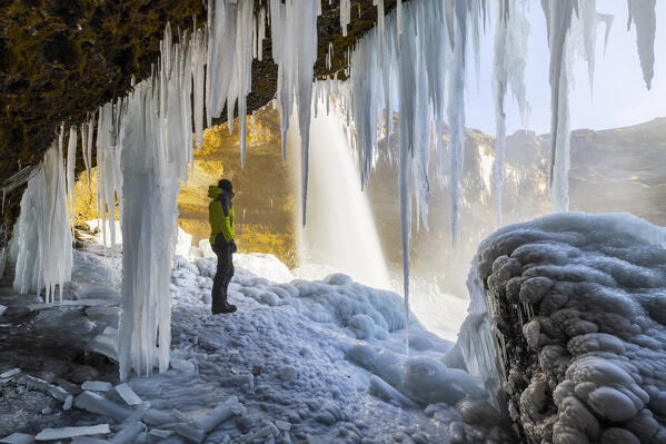 A man at Kvernufoss waterfall under stalactites, Skogar, Sudurland, Iceland, Northern Europe