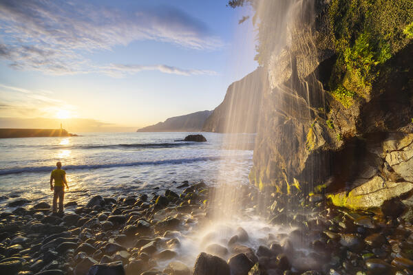A man observes sunrise at a waterfall in Seixal black sand beach, Seixal, Porto Moniz, Madeira, Portugal, Europe (MR)