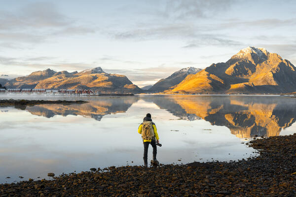 A photographer observes mountains and rorbuer in a Fjord during sunset, Leknes, Vestvagoy, Nordland, Lofoten Islands, Norway, Northern Europe (MR)