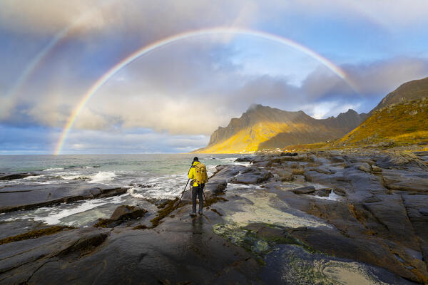 A photographer portrays rainbow at Vikten beach during sunset, Flakstad, Moskenesoya, Nordland, Lofoten Islands, Norway, Northern Europe