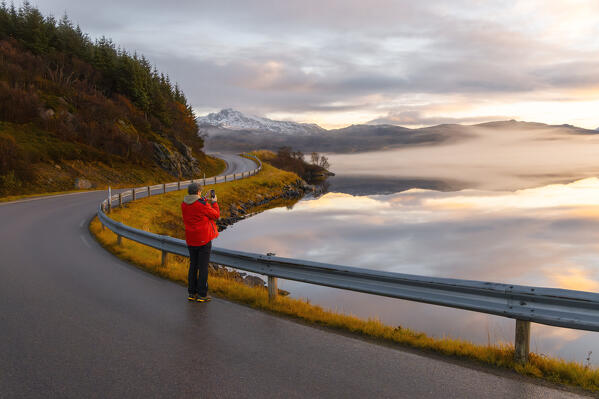 A tourist photographs reflections and mist in Vagspollen during sunset along the road to Uttakleiv beach, Leknes, Vestvagoy, Nordland, Lofoten Islands, Norway, Northern Europe