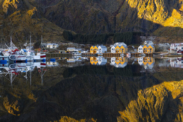 Reflections of houses and mountains in the water at Ballstad village during sunrise, Vestvagoy, Nordland, Lofoten Islands, Norway, Northern Europe