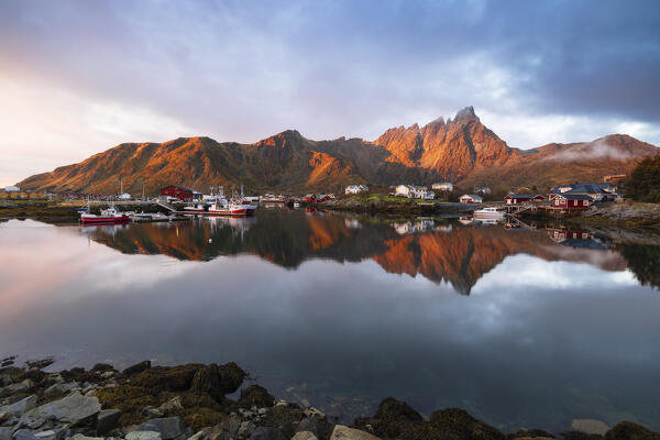 Reflections of houses and mountains in the water at Ballstad village during sunrise, Vestvagoy, Nordland, Lofoten Islands, Norway, Northern Europe