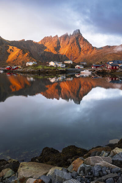 Reflections of houses and mountains in the water at Ballstad village during sunrise, Vestvagoy, Nordland, Lofoten Islands, Norway, Northern Europe