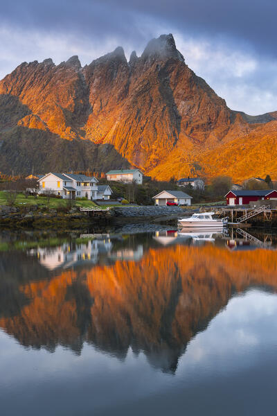 Reflections of houses and mountains in the water at Ballstad village during sunrise, Vestvagoy, Nordland, Lofoten Islands, Norway, Northern Europe