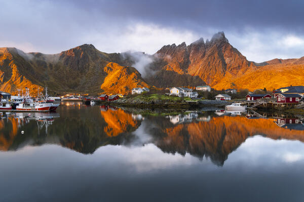 Reflections of houses and mountains in the water at Ballstad village during sunrise, Vestvagoy, Nordland, Lofoten Islands, Norway, Northern Europe