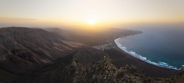 Aerial and panoramic view of a man observes Famara beach from Risco de Famara at sunset, Famara, Las Palmas, Canary Islands, Macaronesia, Spain, Western Europe