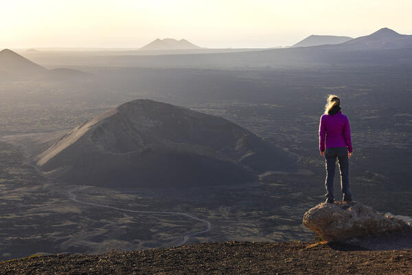 A woman observes Volcan El Cuervo at sunset from Montana Negra, Tinajo, Las Palmas, Canary Islands, Macaronesia, Spain, Western Europe