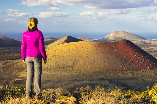 A woman observes Caldera Colorada at sunset from Montana Negra, Tinajo, Las Palmas, Canary Islands, Macaronesia, Spain, Western Europe