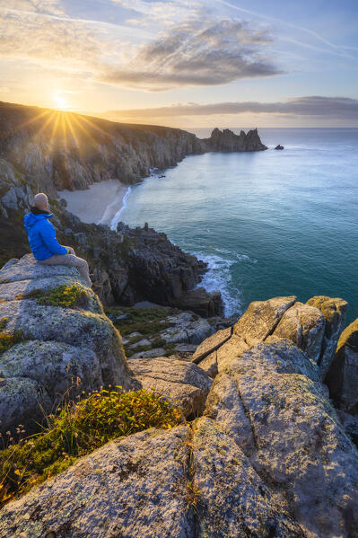 A tourist at Logan Rock and Pedn Vounder beach during sunrise, St Levan, Treen, Penzance, Cornwall, England, Great Britain, United Kingdom
