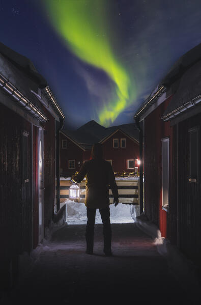 Tourist observes Northern Lights with a lantern at Skreda Nasjonale Turistvager Rorbuer, Leknes, Vestvagoy, Lofoten, Nordland, Norway, Scandinavia, Nothern Europe
